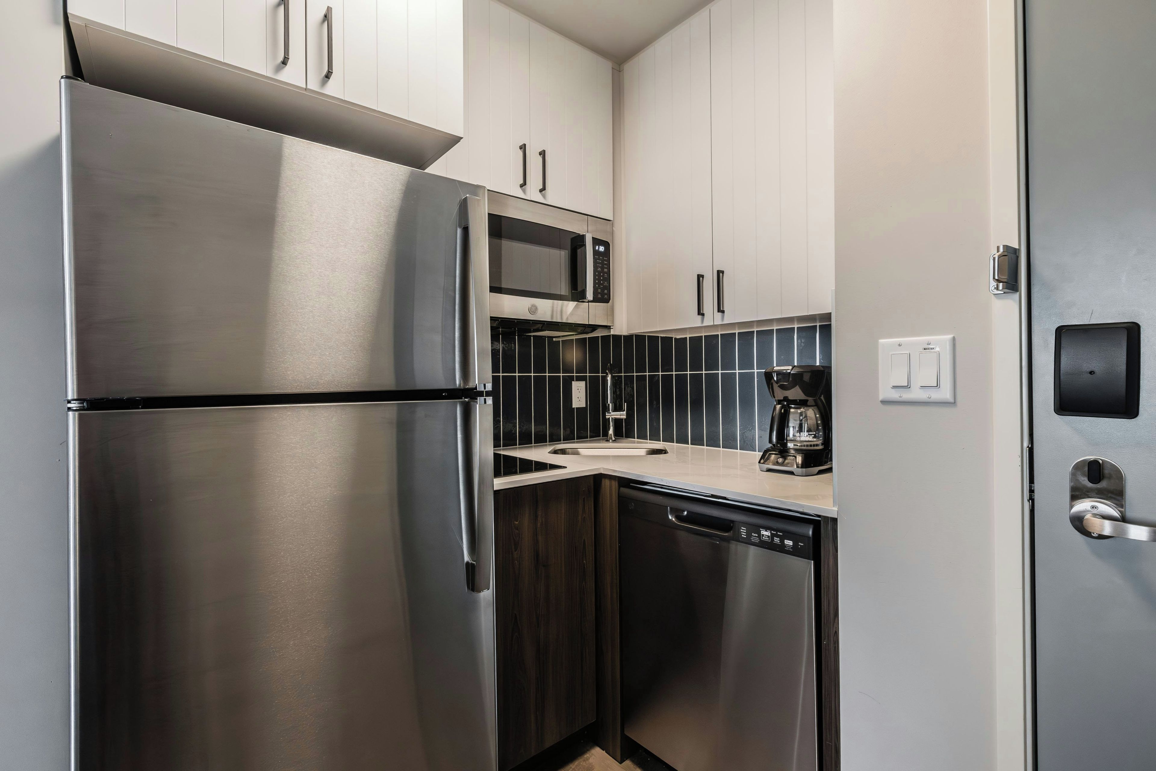 Una cocina compacta con electrodomésticos de acero inoxidable, incluyendo un refrigerador, microondas y cafetera.