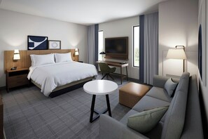 Et hotelværelse med seng, skrivebord, fjernsyn, sofa og et lille bord.
