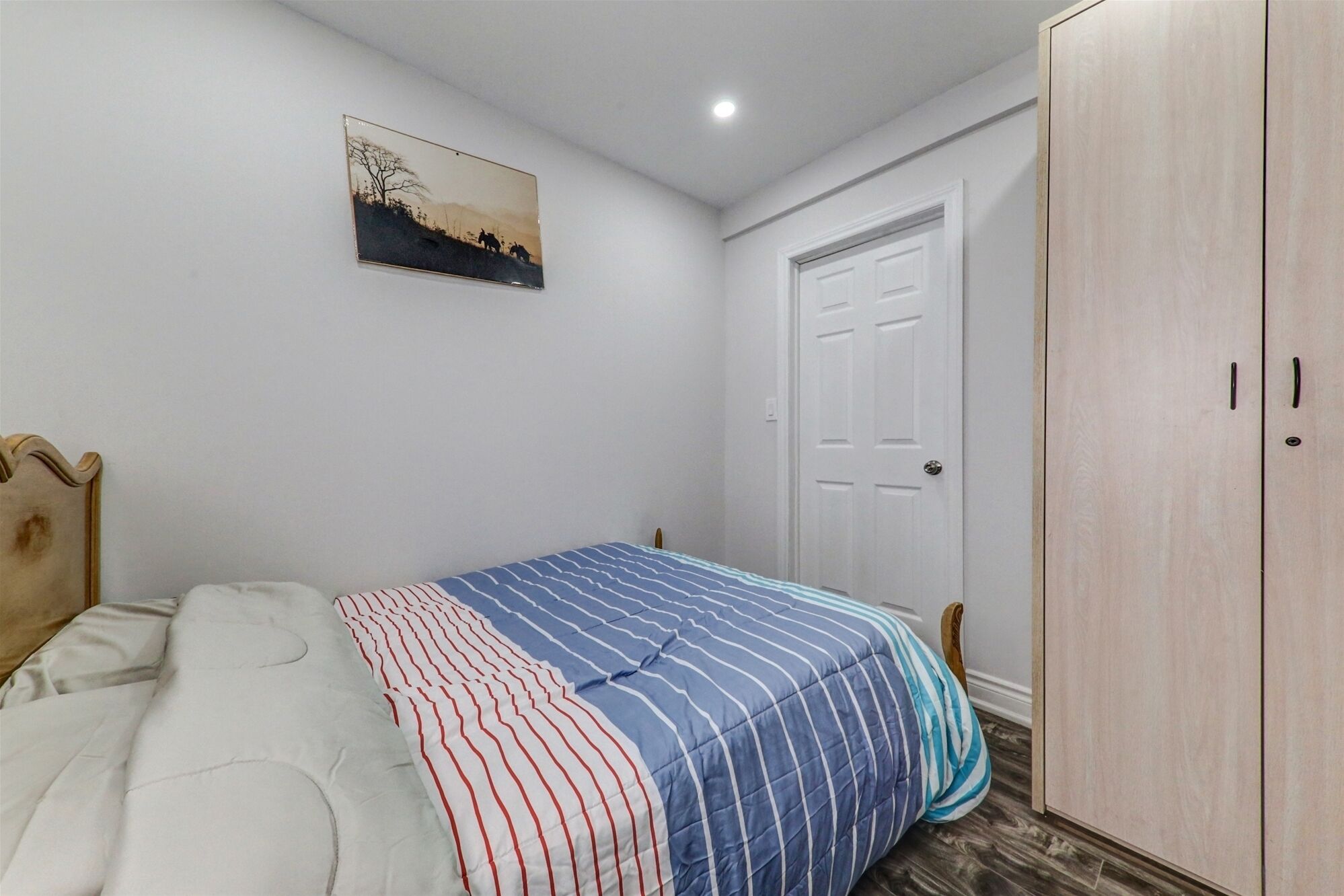 Une chambre à coucher comprenant un lit, une armoire, une porte et un tableau accroché au mur.
