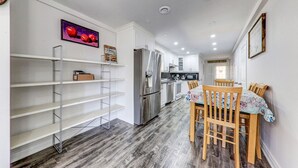 A modern kitchen with white cabinets, a stainless steel refrigerator, and a microwave. There is a dining area with a table and chairs, and a wooden floor. - 3 bedroom house near scugog lake (Caesarea)