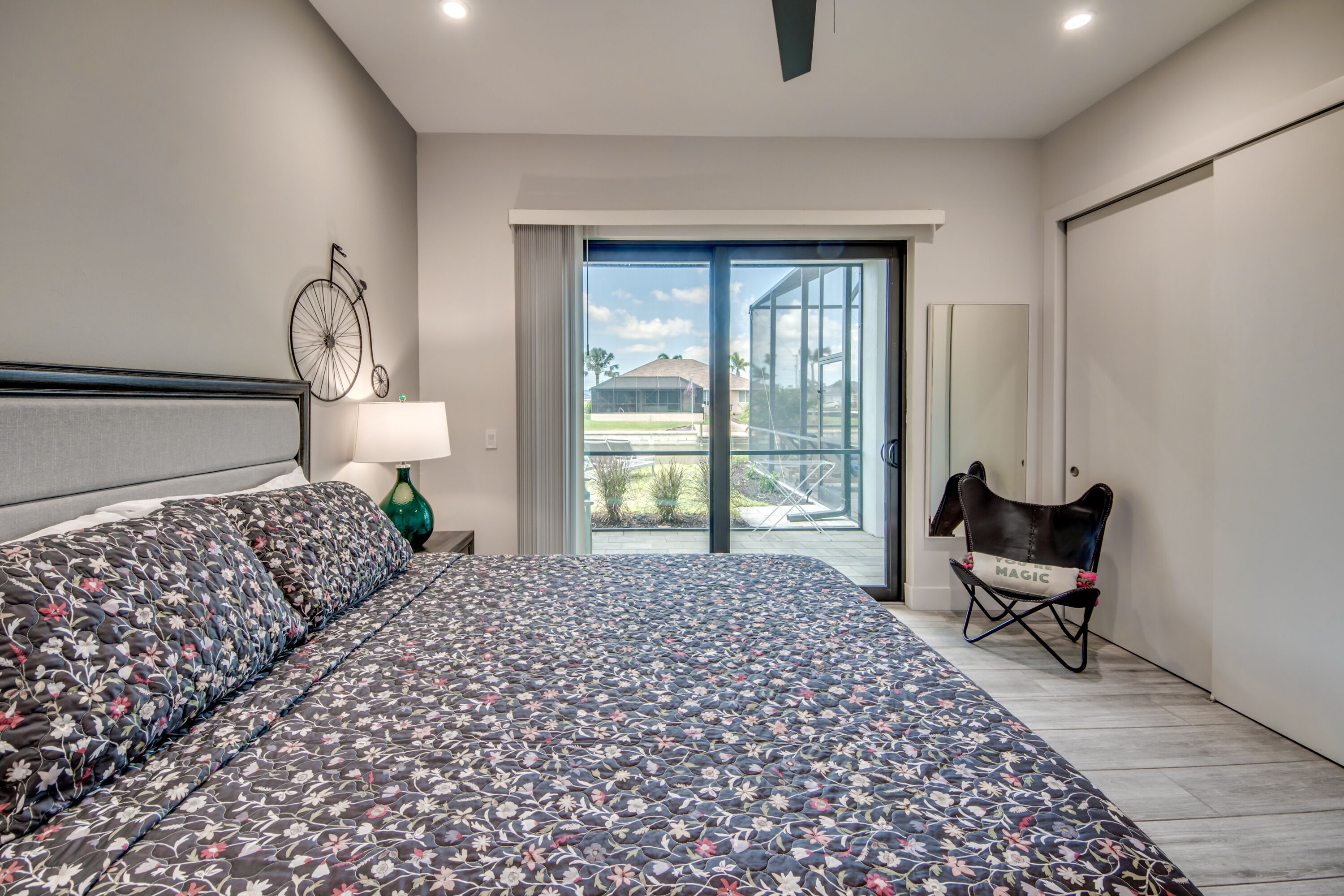 A bedroom with a large bed, a bicycle decoration on the wall, a chair, and a view of the outdoors through a sliding door.
