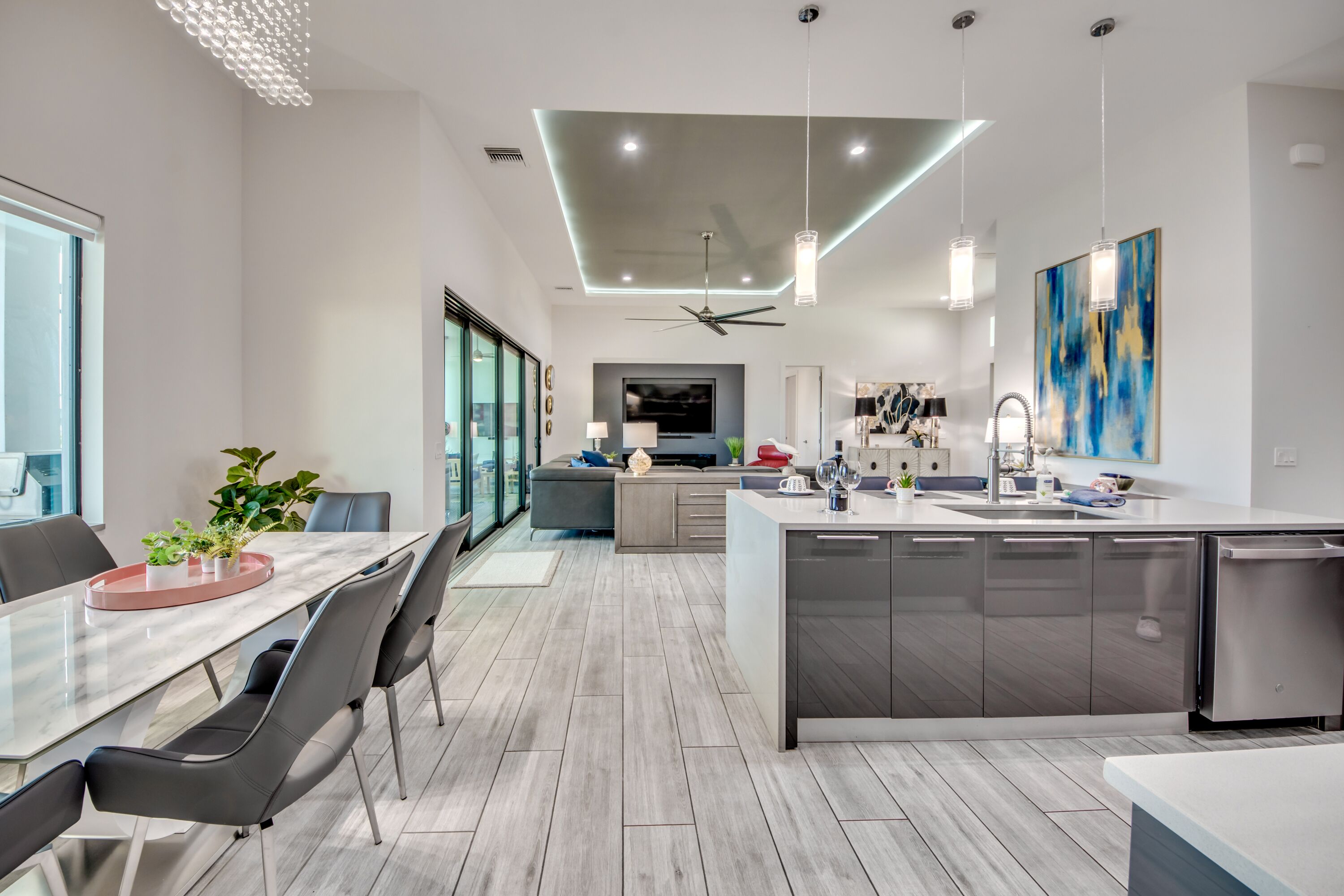 Una cocina moderna con una isla central, un comedor con mesa de vidrio y una sala de estar con sofá y televisor.