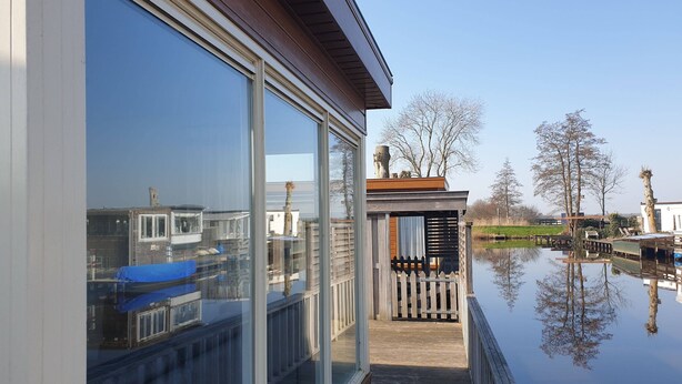A modern house with large glass windows, a wooden deck, and a view of a calm lake with boats. - Splendid Chalet in Bantega With a Jettty (Bantega)