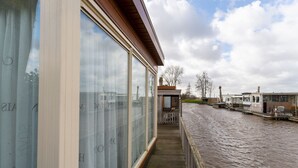 A wooden deck overlooking a canal with a row of houses in the background. - Splendid Chalet in Bantega With a Jettty (Bantega)