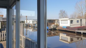 A view through a window of a building with a reflection of a water body and mobile homes. - Splendid Chalet in Bantega With a Jettty (Bantega)