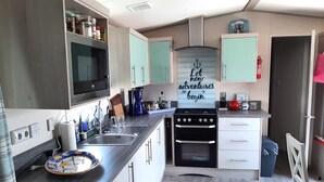 Une cuisine compacte équipée d’un four à micro-ondes, d’une cuisinière et d’un évier, avec des meubles de couleur vert clair et une citation inspirante sur le mur.