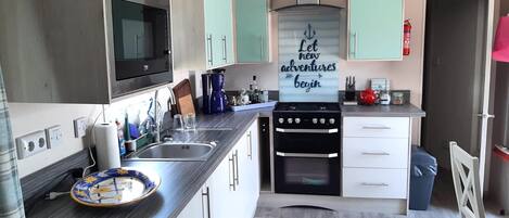 A compact kitchen with a microwave, stove, and sink, light green cabinets, and a motivational quote on the wall.