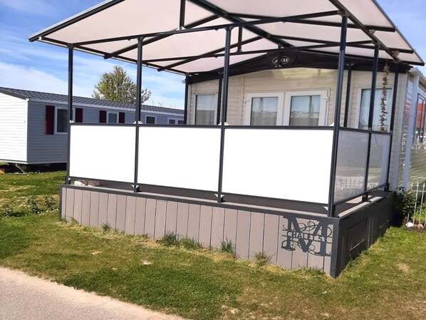 A covered outdoor area with a metal frame and a large white panel, likely a patio or lounge space, adjacent to a building with a window and a door.