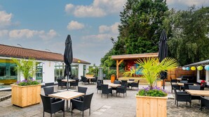 Un espace extérieur aménagé en terrasse, avec des tables et des chaises en bois, entouré de plantes en pot et de parasols.