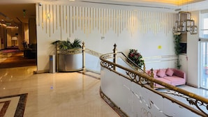 A modern hotel lobby with a marble floor, a reception desk, a staircase with a golden railing, and a pink sofa. - Ivory Inn Hotel Doha (Doha)