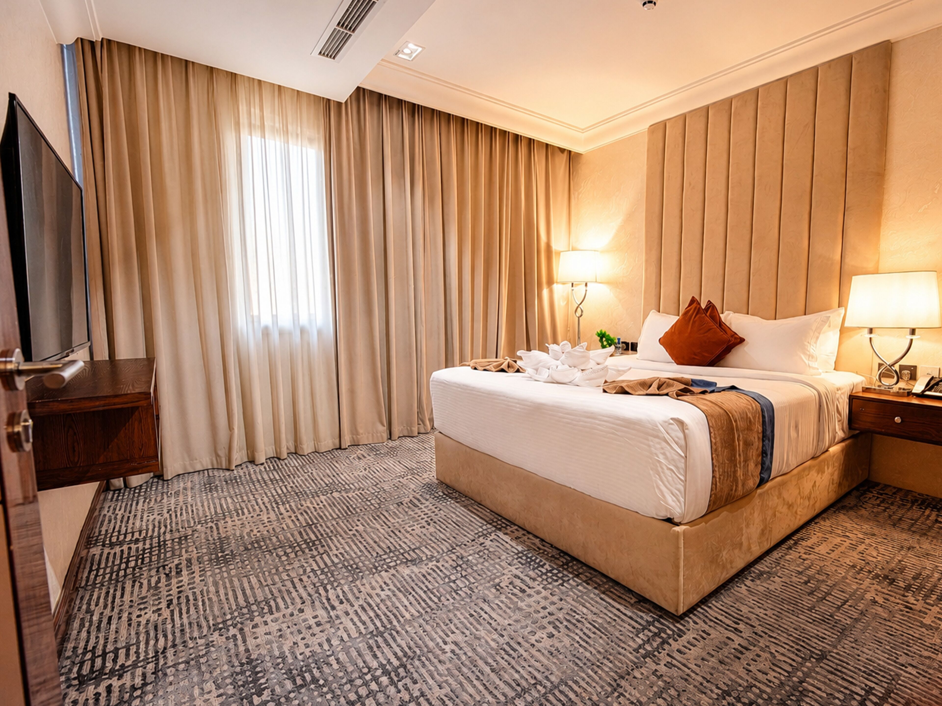Habitación de hotel con una cama grande, televisión, escritorio y ventana con cortinas.