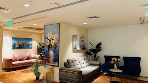 A modern lobby with a grey sofa, a pink sofa, and two blue armchairs. There are paintings on the walls and a large vase with flowers on a table. - Ivory Inn Hotel Doha (Doha)