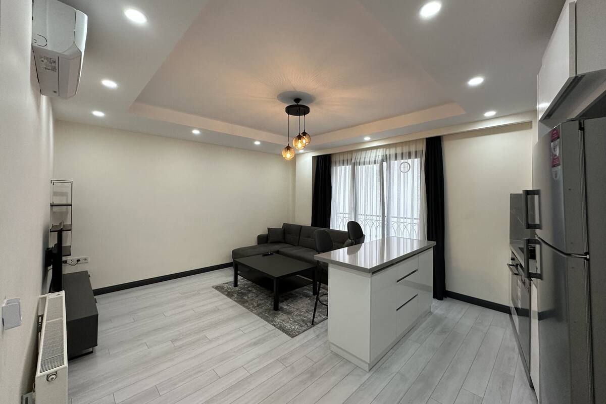A modern kitchen with a built-in refrigerator, a dining area with a sofa and table, and a large window with curtains.