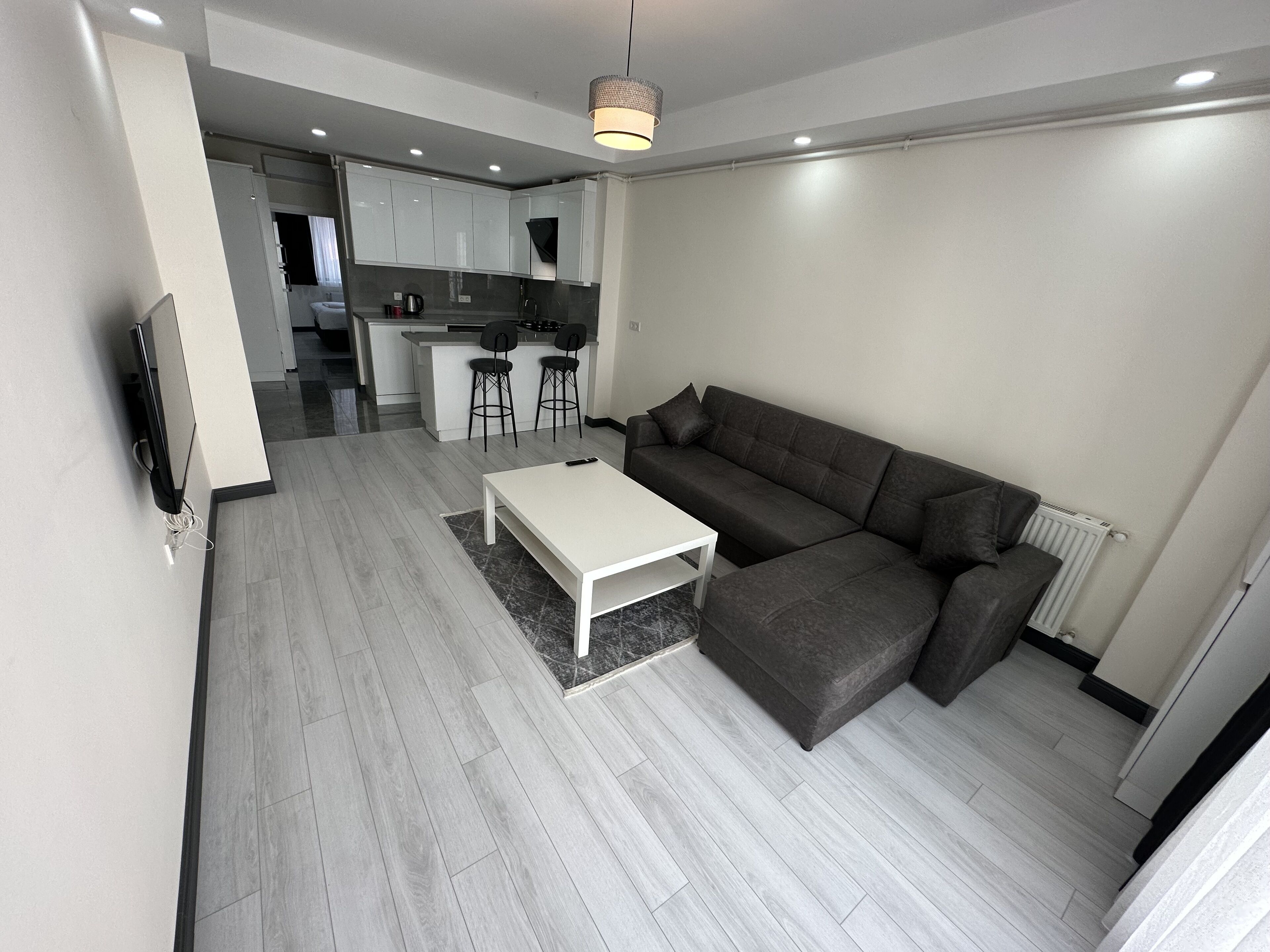 Ein modernes Wohnzimmer mit einem grauen Sofa, einem weißen Couchtisch und einer Küchenzeile im Hintergrund.