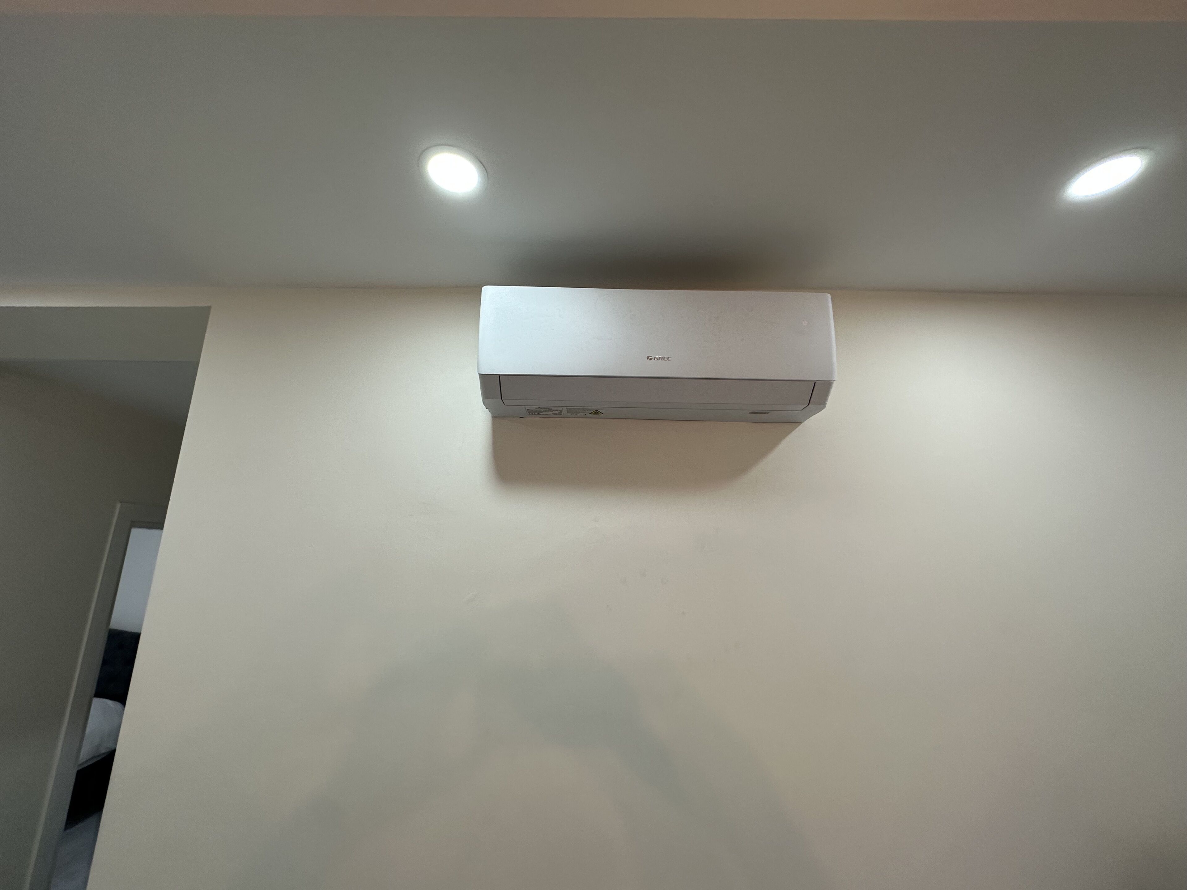 A white air conditioning unit mounted on a plain wall with two ceiling lights above it.
