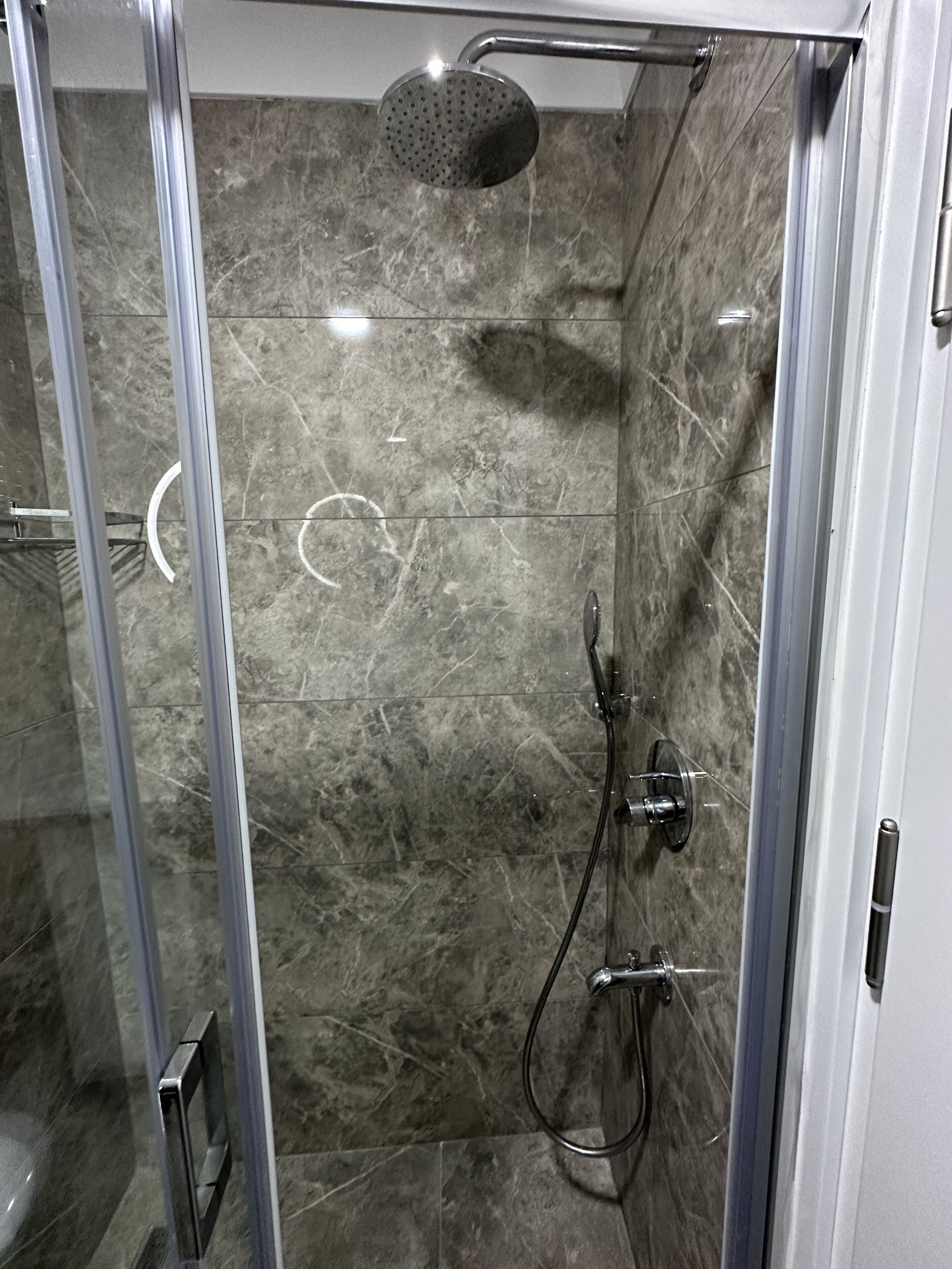 A glass-enclosed shower with a handheld showerhead and a wall-mounted faucet.