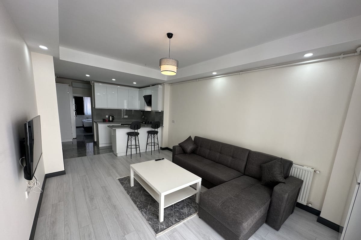 A modern living room with a grey sofa, a white coffee table, and a kitchen in the background.