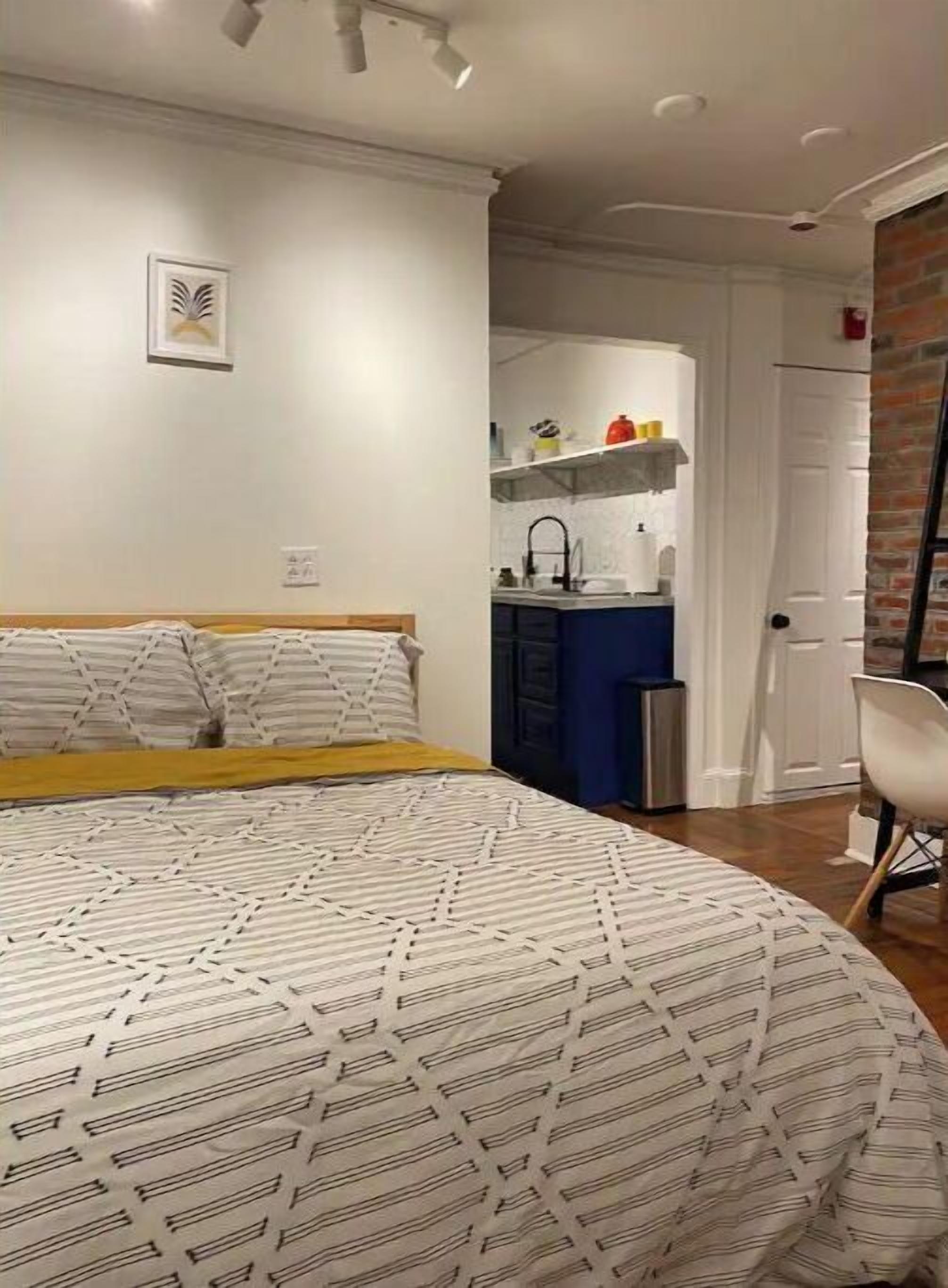 A bedroom with a bed, a small kitchenette, and a door leading to a bathroom.