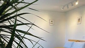 Une chambre avec un plancher en bois, un lit avec une literie à rayures et une plante au premier plan.