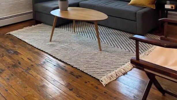 Un salon moderne avec un canapé gris, des coussins jaunes, une table basse ronde en bois et une grande fenêtre avec des stores.