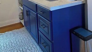 Une cuisine compacte avec un meuble bleu, un plan de travail blanc, un pare-feu hexagonal et une petite étagère avec des récipients rouges et jaunes.