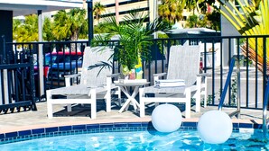 A poolside area with white lounge chairs, a small table with drinks, and two white floating balls. - Devon Shores - Triple Queen (Clearwater)