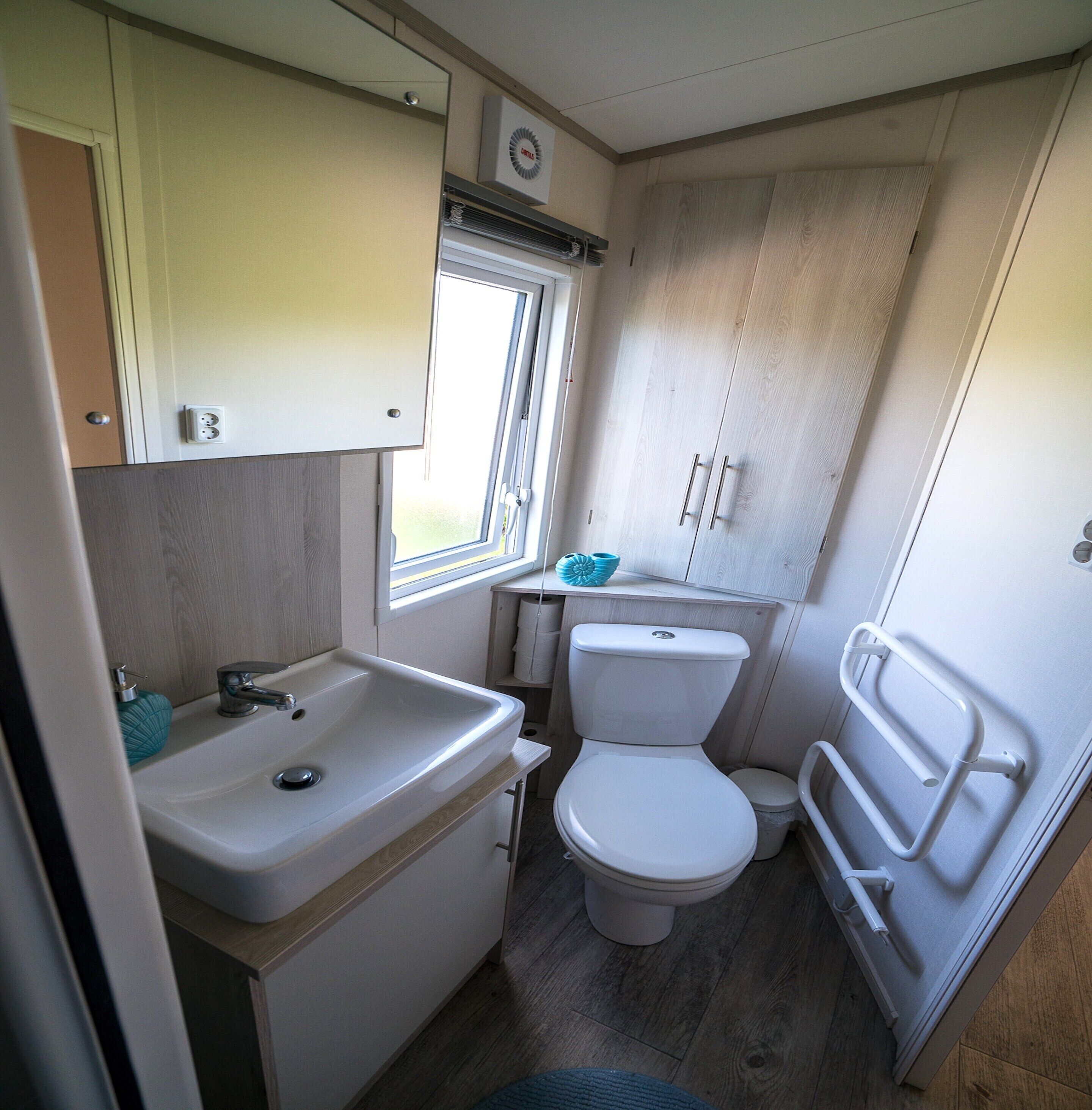 A compact RV bathroom with a sink, toilet, and window.