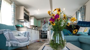 A cozy living room with a sofa, a coffee table with a vase of flowers, and a kitchen in the background. - Chalet in Oostkapelle Near the Beach (Oostkapelle)