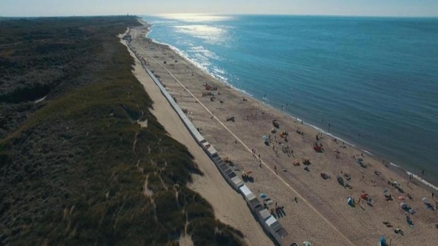 An aerial view of a beach with a long stretch of beach chairs and umbrellas, a clear sky, and the ocean. - Chalet in Oostkapelle Near the Beach (Oostkapelle)
