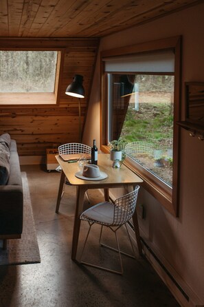 A cozy dining area with a wooden table, metal chairs, a laptop, a wine bottle, and a potted plant.