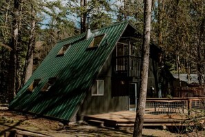 Een chalet met schuin dak, een balkon en een omheind buitengebied, omringd door bomen.