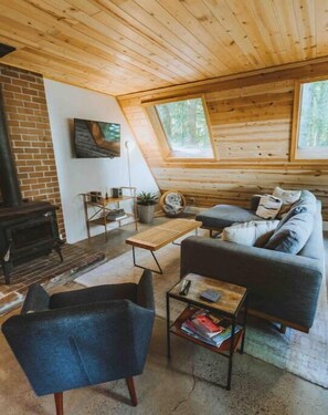 Een gezellig cabin interieur met een open haard, een bank, een bijzettafeltje en een boekenkast.