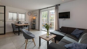 Een moderne woonkamer met een bank, een eettafel en een aan de muur bevestigde televisie.