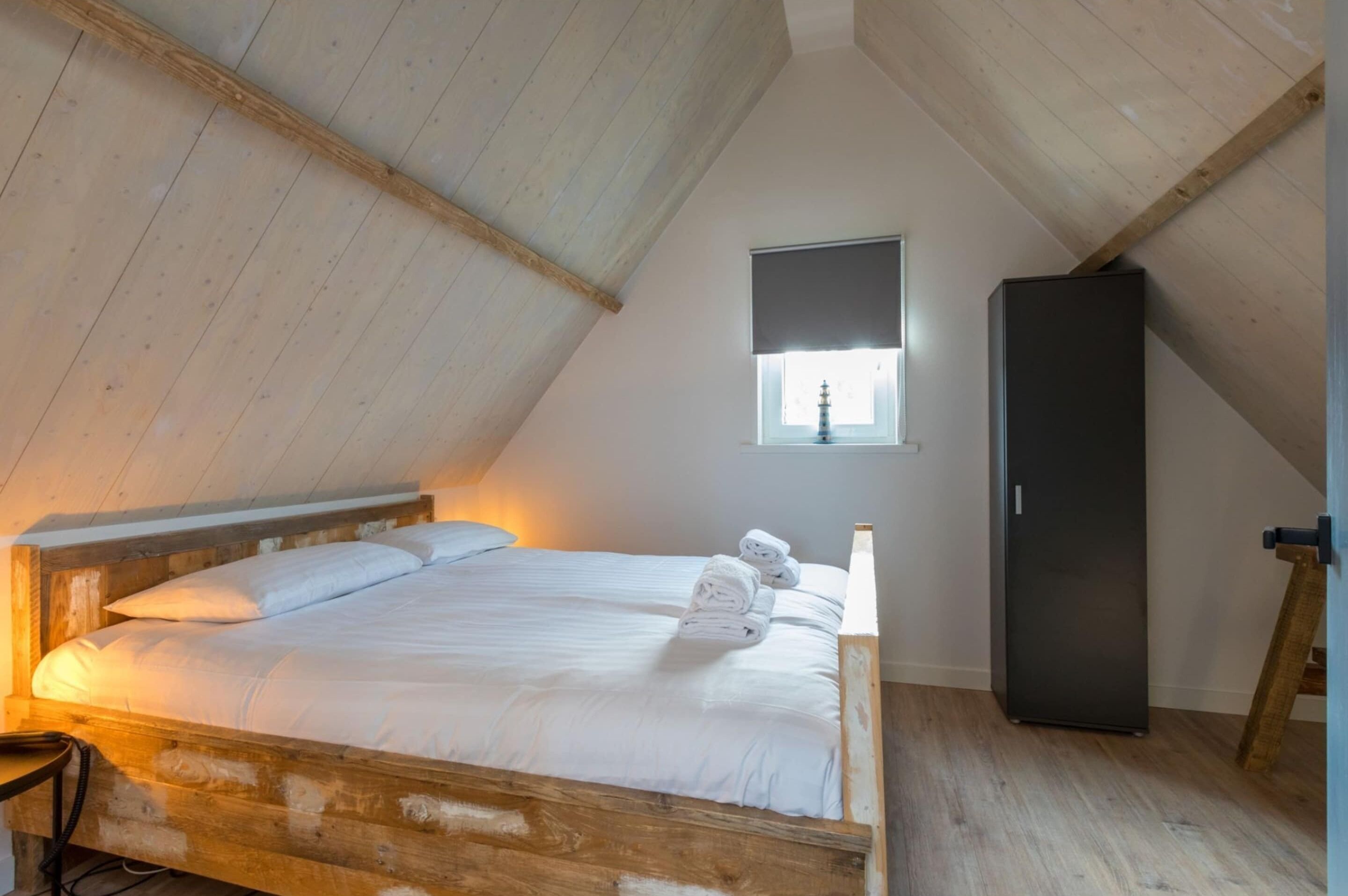 A bedroom with a wooden bed, a window with a view, and a black wardrobe.