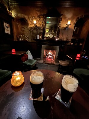A cozy bar area with a fireplace, two glasses of beer, and a lit candle on a wooden table. - Ennis, 4 minute walk to Downtown (Ennis)