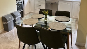 A modern kitchen with white cabinets, a glass dining table with black chairs, and a view of the garden through the window. - Ennis, 4 minute walk to Downtown (Ennis)
