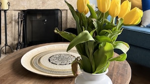 A room with a round wooden table, a white vase with yellow tulips, a fireplace, a blue sofa, and a framed mirror on the wall. - Ennis, 4 minute walk to Downtown (Ennis)