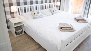 A neatly made bed with white bedding and two pillows, a bedside table with a lamp, and a small storage basket.