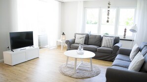 A modern living room with a flat-screen TV, a grey sofa set, a white coffee table, and a white side table with a lantern.