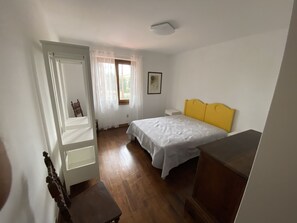 Ein Schlafzimmer mit einem Bett, einem Sessel, einem kleinen Tisch und einem Fenster mit Vorhängen.