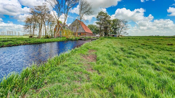 A canal with a wooden bridge, a grassy field, and a traditional house with a red roof. - Farmhouse in Suwald With Hot Tub (Suwâld)