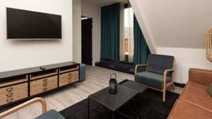 Ett modernt vardagsrum med en platt-TV, ett träskåp med lådor, en blå fåtölj, en brun soffa och ett svart soffbord.