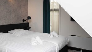 Ett hotellrum med en stor säng, en sänggavel, ett nattduksbord, en lampa och ett fönster med gardiner.