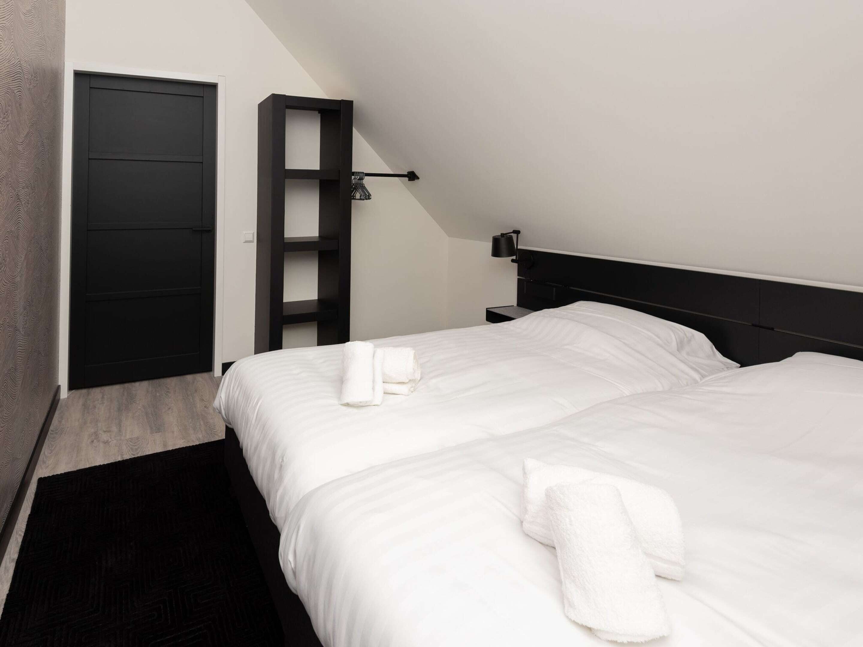 A modern hotel room with a large bed, a built-in wardrobe, and a bedside table with a lamp.