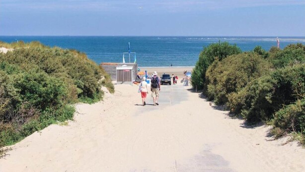 En sandstig som leder till en strand med en liten byggnad och ett livräddartorn.
