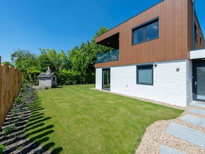 Een modern huis met een witte gevel en een bruin dak, een verzorgd gazon en een houten omheining.
