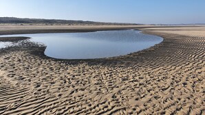 A sandy beach with a calm water body, likely a small lake or pond, surrounded by dunes. - Lovely Holiday Home in a Quiet Location (Kamperland)