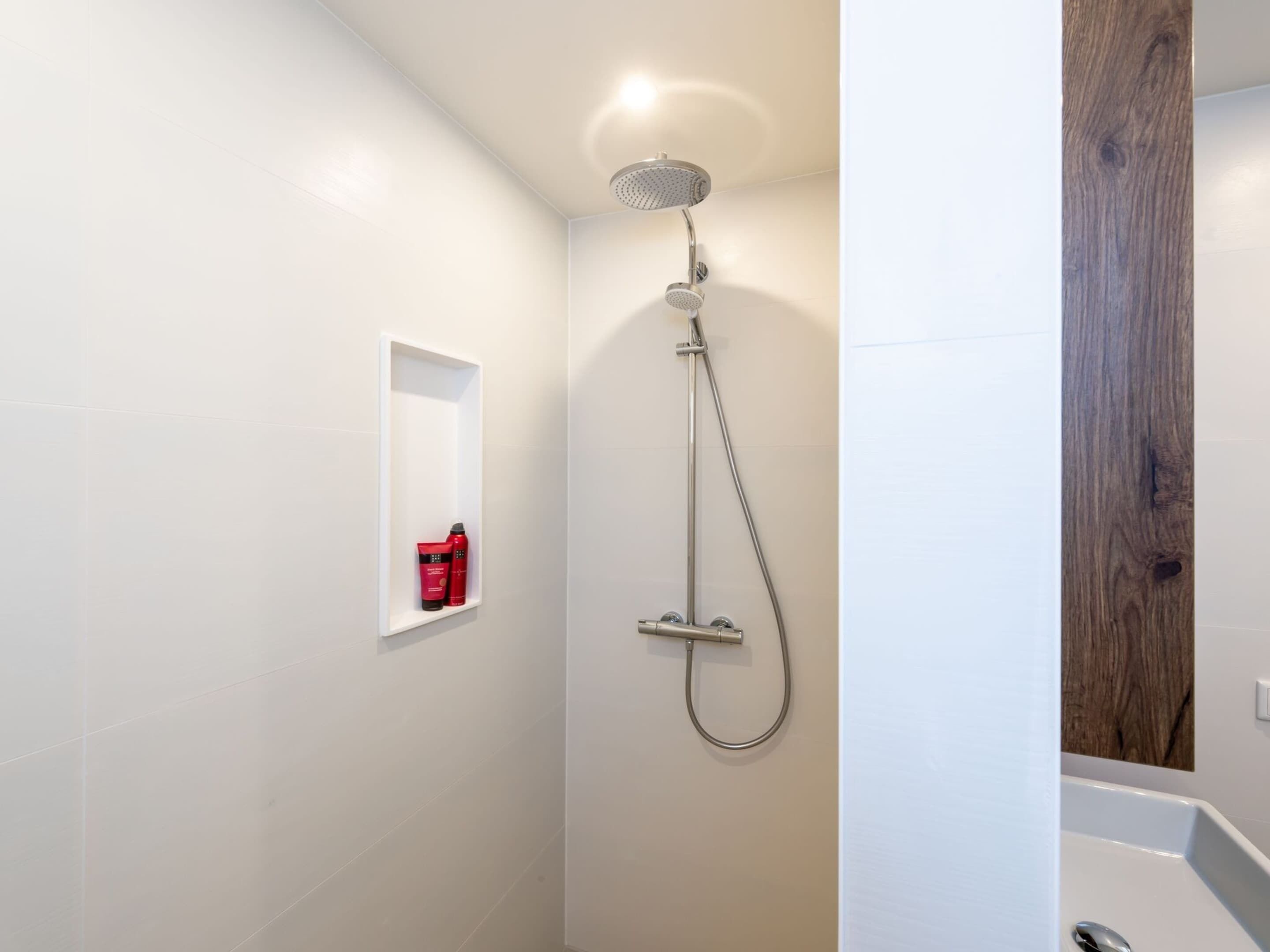 A modern bathroom with a shower, a small shelf with toiletries, and a wooden accent wall.