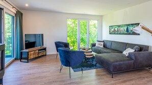 A modern living room with a flat-screen TV, a grey sofa, blue chairs, and a wooden coffee table. - Lovely Holiday Home in a Quiet Location (Kamperland)