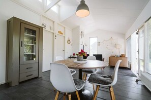 A modern dining area with a round wooden table, white chairs, and a cabinet with glass doors. - Beautiful Holiday Home in Ouddorp With Balcony (Ouddorp)